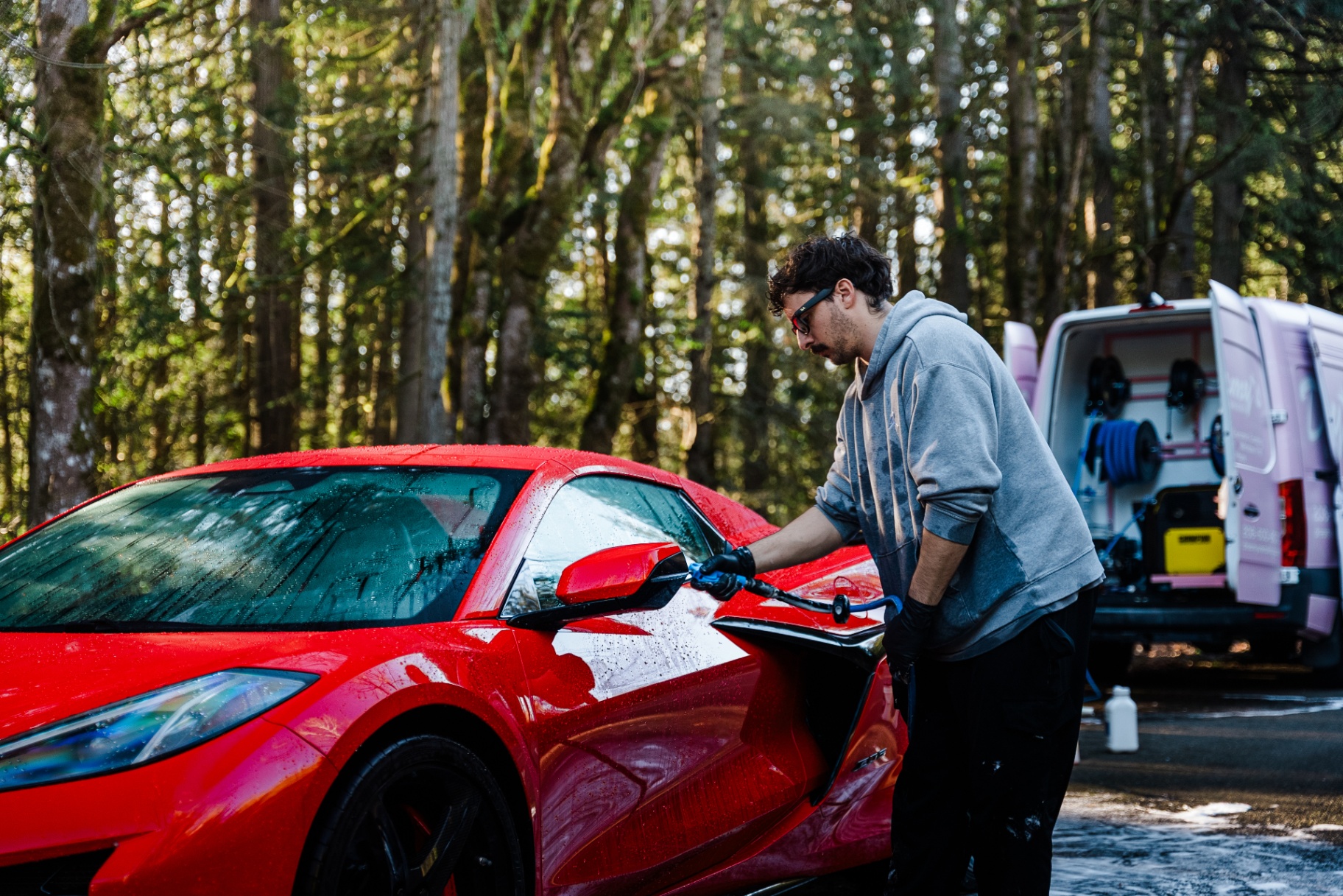 A detailer's gloved hand gliding a foamy wash mitt over a glossy car panel.